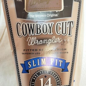 May include: A product tag for Wrangler Cowboy Cut jeans. The tag features the Wrangler logo, the text "Cowboy Cut," and "Slim Fit." It also includes a "Made in the USA" label and a 14-year guarantee seal.
