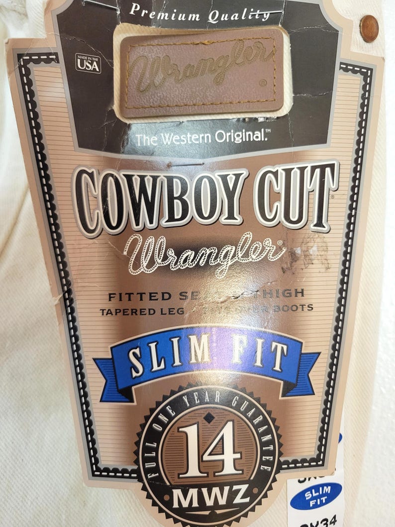May include: A product tag for Wrangler Cowboy Cut jeans. The tag features the Wrangler logo, the text "Cowboy Cut," and "Slim Fit." It also includes a "Made in the USA" label and a 14-year guarantee seal.