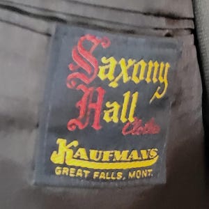 May include: A black label with the text "Saxony Hall" in red and yellow lettering. Below the text is "Kaufman's" in yellow lettering and "Great Falls, Mont." in white lettering.
