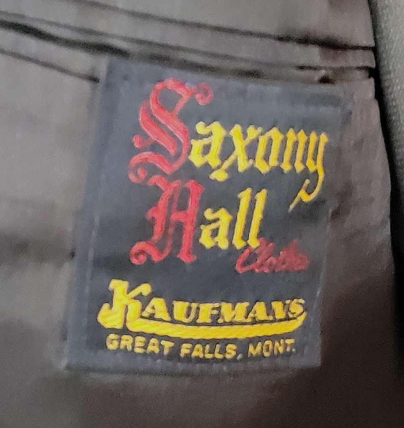 May include: A black label with the text "Saxony Hall" in red and yellow lettering. Below the text is "Kaufman's" in yellow lettering and "Great Falls, Mont." in white lettering.