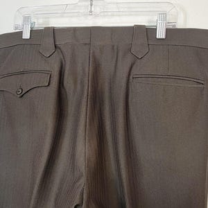 May include: A pair of brown dress trousers with a subtle pinstripe pattern. The trousers have two back pockets and a zip fly.