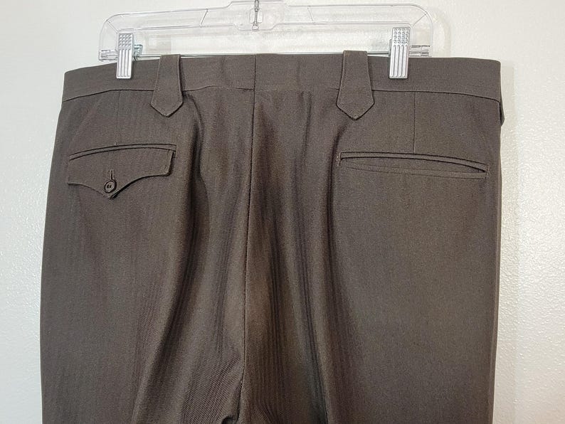 May include: A pair of brown dress trousers with a subtle pinstripe pattern. The trousers have two back pockets and a zip fly.