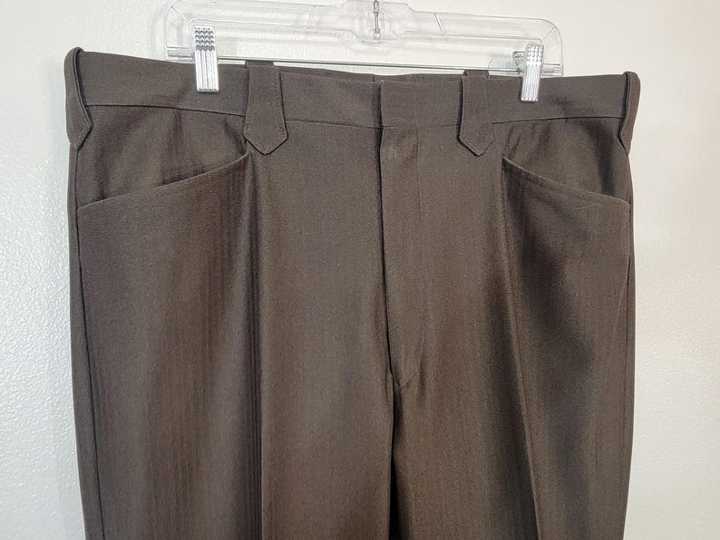 May include: A pair of brown dress trousers with a subtle pinstripe pattern. The trousers have two front pockets and two back pockets.