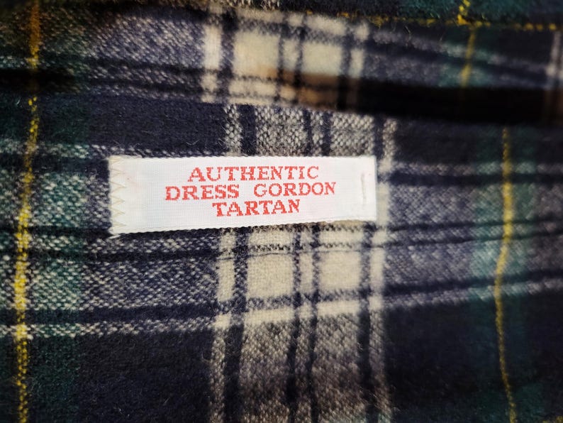 Pu&ograve; includere: Un tessuto con motivo tartan Dress Gordon nei toni del blu scuro, verde bosco, bianco e sottili linee gialle. Un'etichetta rettangolare bianca &egrave; cucita sul tessuto con il testo rosso AUTHENTIC DRESS GORDON TARTAN.