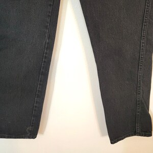 Puede incluir: Primer plano de unos vaqueros de mezclilla negros. Los vaqueros tienen un dise&ntilde;o cl&aacute;sico de cinco bolsillos, con un corte de pierna recta. El denim es de color negro liso y las costuras son visibles a lo largo de las costuras.