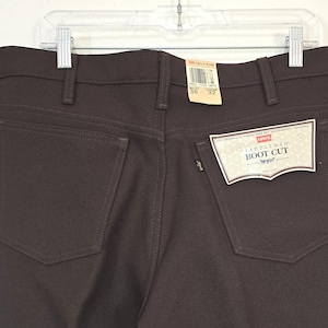 May include: Dark brown Levi's Saddleman boot cut jeans with a high waist and belt loops. The jeans feature two back pockets, a small black tab on the right pocket, and original paper tags attached, including one marked waist 36 and length 32.