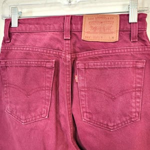 May include: Close-up of the back of a pair of burgundy Levi's jeans. The jeans are hanging on a clear hanger. The Levi Strauss & Co. label is visible on the back waistband. The jeans have two back pockets and a small red Levi's tag.