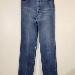 May include: Vintage blue denim jeans with a high waist and straight leg. The jeans have a classic five-pocket design, a button and zipper closure, and belt loops. The denim has a faded appearance.