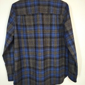 K&ouml;nnte beinhalten: Ein blau-schwarz-graues Flanellhemd mit Karomuster. Das Hemd h&auml;ngt an einem wei&szlig;en Kleiderb&uuml;gel. Das Karomuster ist ein klassisches Design mit einem Button-Down-Kragen und langen &Auml;rmeln.