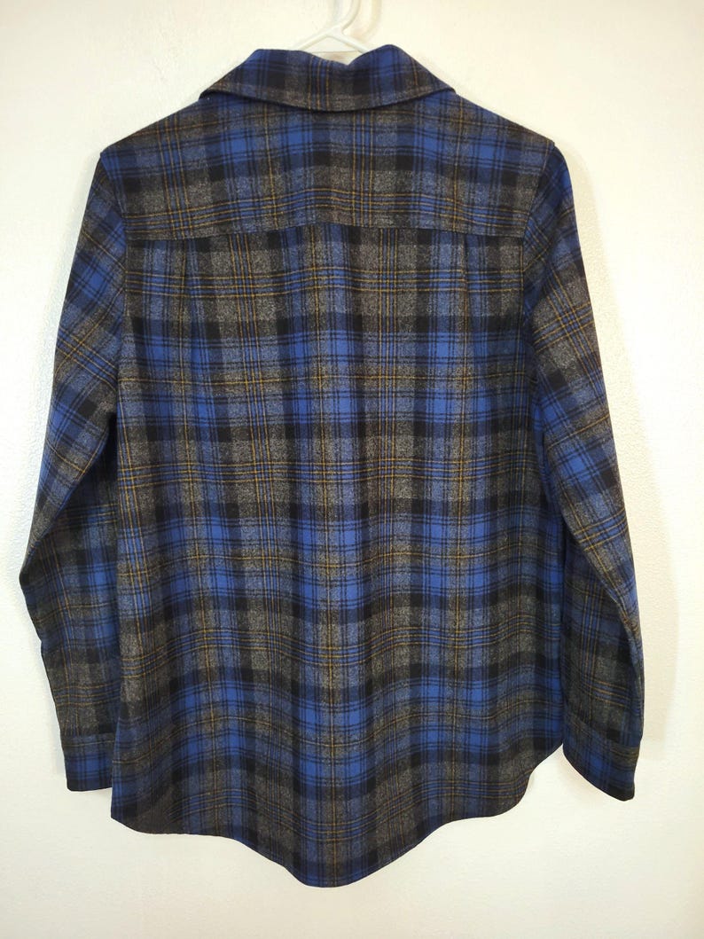 K&ouml;nnte beinhalten: Ein blau-schwarz-graues Flanellhemd mit Karomuster. Das Hemd h&auml;ngt an einem wei&szlig;en Kleiderb&uuml;gel. Das Karomuster ist ein klassisches Design mit einem Button-Down-Kragen und langen &Auml;rmeln.