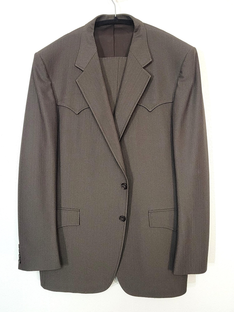 May include: A brown suit jacket with a single-breasted closure and two flap pockets. The jacket has a subtle herringbone pattern and a pointed collar.
