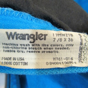 Puede incluir: Una etiqueta de ropa Wrangler blanca con costuras azules. La etiqueta tiene el texto "Wrangler", "17MWZTB", "7/8 X 36", "Machine wash with like colors, only non-chlorine bleach when needed. Tumble dry, remove promptly.", "MADE IN USA", "100% COTTON", "H761-016" y "0 84084 1 0696 4".