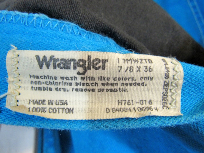 Puede incluir: Una etiqueta de ropa Wrangler blanca con costuras azules. La etiqueta tiene el texto "Wrangler", "17MWZTB", "7/8 X 36", "Machine wash with like colors, only non-chlorine bleach when needed. Tumble dry, remove promptly.", "MADE IN USA", "100% COTTON", "H761-016" y "0 84084 1 0696 4".