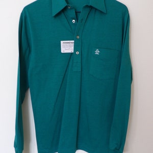 May include: Teal long-sleeve polo shirt with a button-down collar and a chest pocket featuring a penguin logo. The shirt has a tag that reads "MUNSINGWEAR". The collar reads "GRAND SLAM".