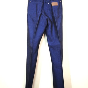 May include: Dark blue denim jeans with a classic five-pocket design. The jeans feature a straight leg cut and a brown leather patch on the back. The Wrangler logo is visible above the patch. The jeans are hanging on a white hanger.