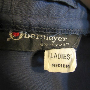 May include: Close-up of a navy blue garment tag with the brand name "Bernmeyer" and the text "LADIES' MEDIUM". The tag also includes the RN number 37037 and a small embroidered logo with a heart.