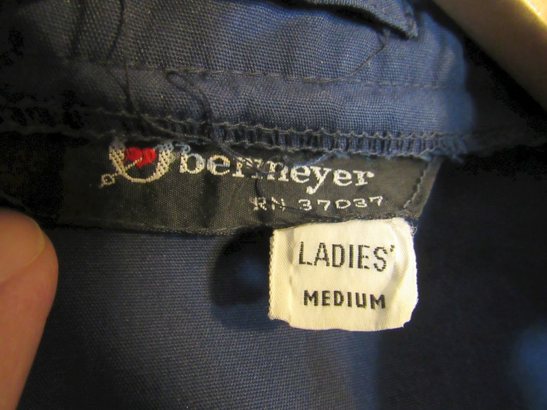 May include: Close-up of a navy blue garment tag with the brand name "Bernmeyer" and the text "LADIES' MEDIUM". The tag also includes the RN number 37037 and a small embroidered logo with a heart.