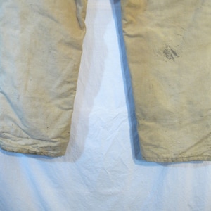 May include: A pair of off-white work pants with a worn and faded appearance. The pants have a straight leg and are made of a durable fabric.