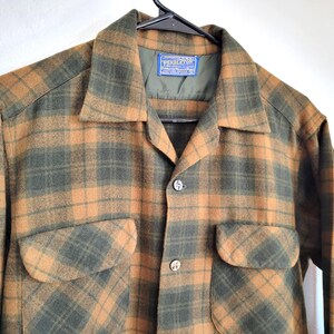 Pode incluir: Uma camisa xadrez vintage em tons de castanho e verde. A camisa apresenta dois bolsos frontais, gola e fechos de bot&atilde;o. A etiqueta Pendleton &eacute; vis&iacute;vel no interior da gola.