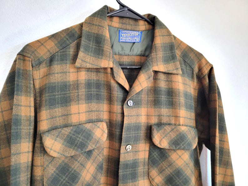 Pode incluir: Uma camisa xadrez vintage em tons de castanho e verde. A camisa apresenta dois bolsos frontais, gola e fechos de bot&atilde;o. A etiqueta Pendleton &eacute; vis&iacute;vel no interior da gola.