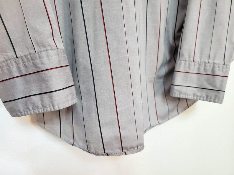 May include: Close-up of a gray button-down shirt with vertical stripes. The shirt features black and burgundy stripes, and the cuffs have matching stripes. The shirt is made of a lightweight fabric.