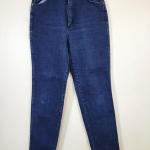 May include: Dark wash denim jeans with a classic five-pocket design. The jeans have a high waist and a straight leg. The jeans are hanging on a white background.