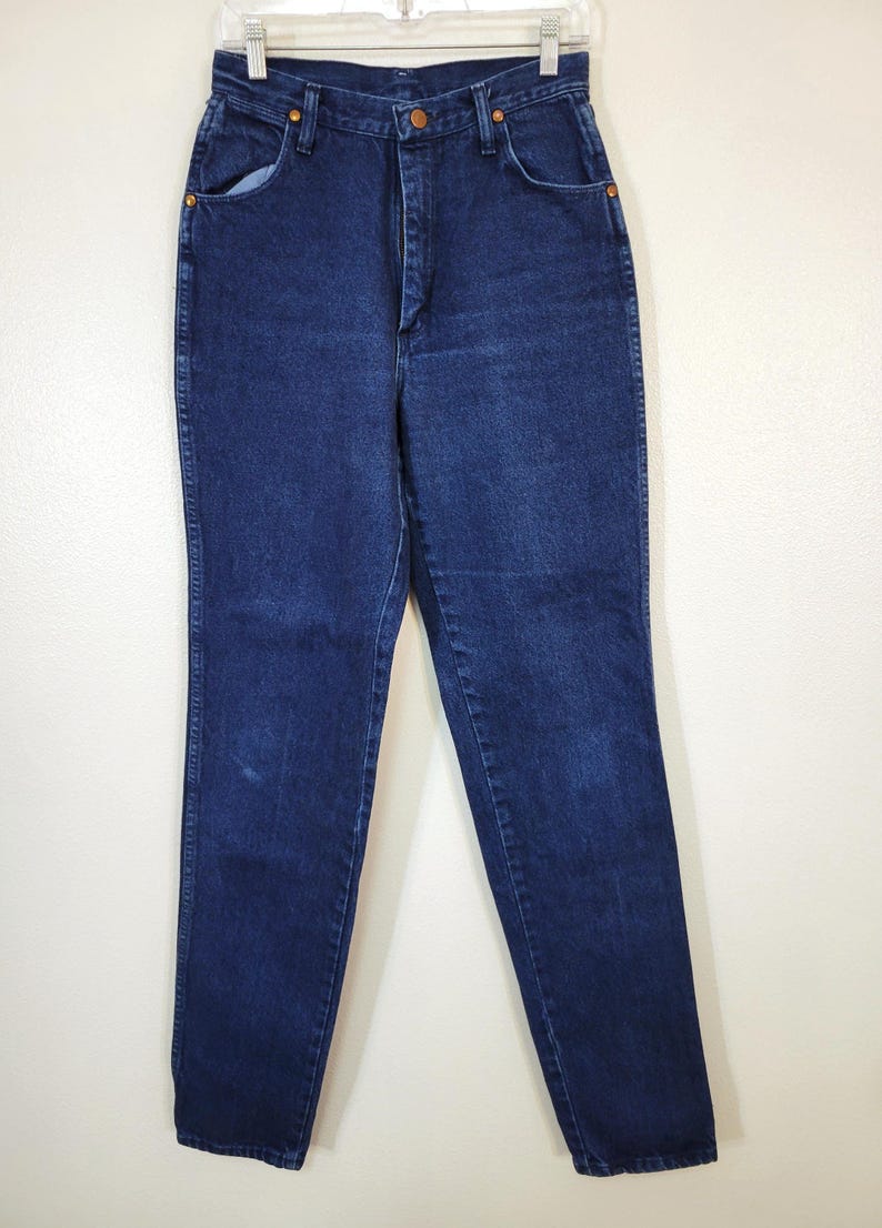 May include: Dark wash denim jeans with a classic five-pocket design. The jeans have a high waist and a straight leg. The jeans are hanging on a white background.
