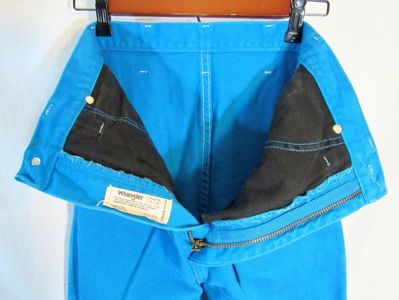 Puede incluir: Un par de pantalones vaqueros azules de mezclilla con cierre de cremallera y una etiqueta Wrangler. Los pantalones est&aacute;n dados vuelta para mostrar el forro negro.