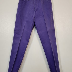 May include: A pair of purple denim pants, displayed on a hanger. The pants have a classic five-pocket design with a button and zipper closure. The denim is a solid, vibrant purple color.