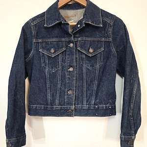 May include: A dark blue denim jacket with a classic design. It has a button-up front, two chest pockets, and long sleeves.
