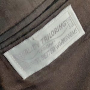 May include: A white label sewn into a brown fabric garment with the text "Quality Tailoring From Our Better Workrooms".