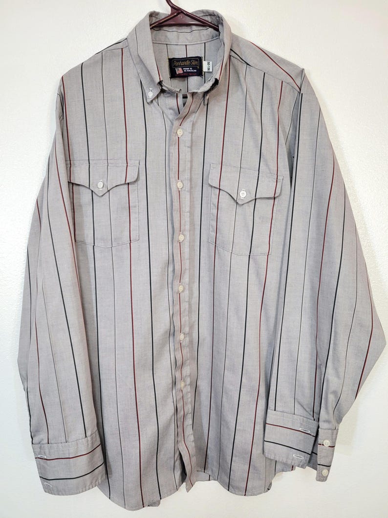 May include: A gray button-down shirt with vertical stripes in black and burgundy. The long-sleeved shirt has two chest pockets and a button-down collar. The brand name "Alexander & Son" is visible on the label.