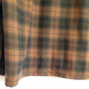 Pode incluir: Close-up de uma camisa de flanela xadrez marrom e verde. A camisa apresenta um padr&atilde;o xadrez cl&aacute;ssico com punho abotoado e um detalhe de bot&atilde;o &uacute;nico. O tecido parece macio e texturizado.