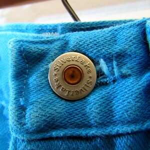 Puede incluir: Primer plano de un jean azul de mezclilla con un bot&oacute;n plateado que dice "Silverlake".