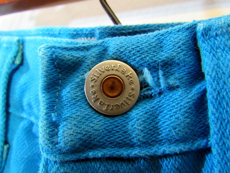 Puede incluir: Primer plano de un jean azul de mezclilla con un bot&oacute;n plateado que dice "Silverlake".