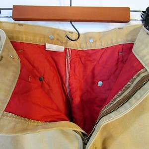 May include: A pair of tan work pants with a red lining and a zipper closure. The pants have multiple pockets and a button fly.