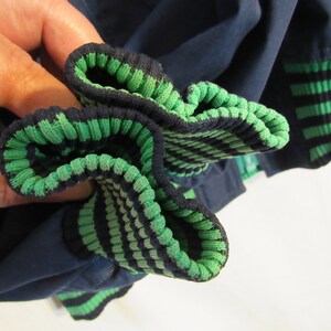 May include: Close-up of a navy blue garment with green and navy striped ribbed cuffs. The cuffs are folded over, revealing the interior green stripes. The fabric appears to be a soft, possibly knit material.