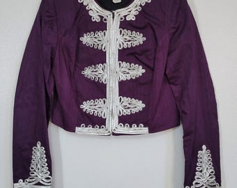 May include: A purple jacket with silver embroidery. The jacket has a round neckline and long sleeves. Silver embroidery trims the collar, front closure, cuffs, and decorative accents. The jacket is hanging on a white hanger.