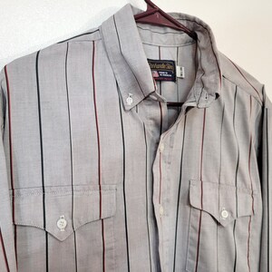 May include: A gray button-down shirt with vertical stripes in black, red, and green. The shirt has two chest pockets and a button-down collar. The brand name "Panhandle Slim" is visible on a tag.