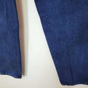May include: Close-up of the lower portion of a pair of dark blue denim jeans. The jeans are slightly faded and have a classic, straight-leg fit. The fabric appears to be a medium-weight denim, suitable for everyday wear. The image shows the legs of the jeans.