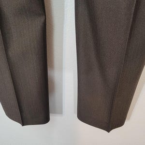 May include: A pair of dark brown trousers with a subtle textured pattern. The trousers are folded in half and laid flat on a white surface.