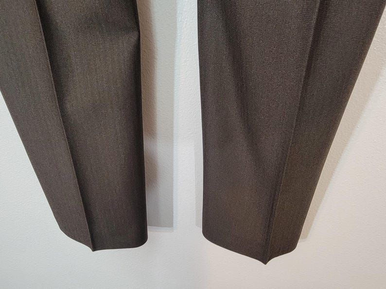 May include: A pair of dark brown trousers with a subtle textured pattern. The trousers are folded in half and laid flat on a white surface.