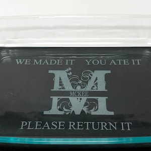 May include: A clear glass baking dish with a rectangular shape and curved edges. Inside, a black insert features the text "WE MADE IT YOU ATE IT" above a monogram and the text "PLEASE RETURN IT".