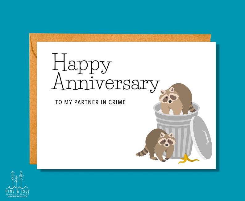 May include: A white card with the text "Happy Anniversary to my partner in crime" and a cartoon illustration of two raccoons in a trash can with a banana peel on the ground.