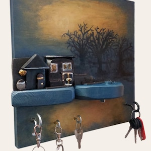 Könnte beinhalten: Ein Schlüsselbrett aus Holz mit einem gemalten Bild eines Hauses und Bäumen in der Abenddämmerung. Das Schlüsselbrett hat zwei blaue Ablagen und fünf Haken zum Aufhängen von Schlüsseln.