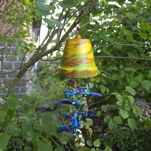 May include: A handmade wind chime with a yellow, green, and brown painted terracotta pot top. Below, blue and purple painted wooden pieces are strung with colorful beads and metallic accents, creating a decorative outdoor ornament.