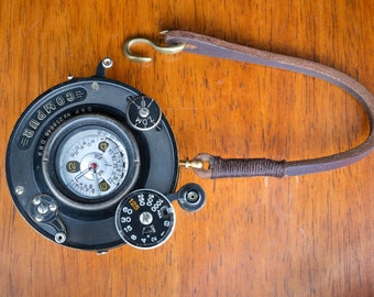 Puede incluir: Un objetivo de cámara negro y plateado con una correa de cuero. El objetivo tiene un dial circular con el texto "DRP No. 258078 COMPUR" y un dial más pequeño con el texto "ZDM".