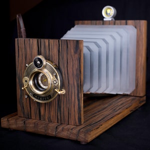 May include: A vintage-style wooden camera with a bellows system and a brass lens. The camera is made of dark wood with a light wood base.