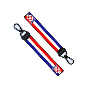 Può includere: Due portachiavi neri con un designo di bandiera croata rosso, bianco e blu. La bandiera presenta un motivo a scacchi e uno stemma.