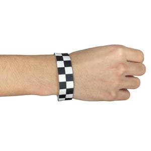 May include: A black and white checkered wristband. The wristband is made of a stretchy material and is worn on a person's wrist.